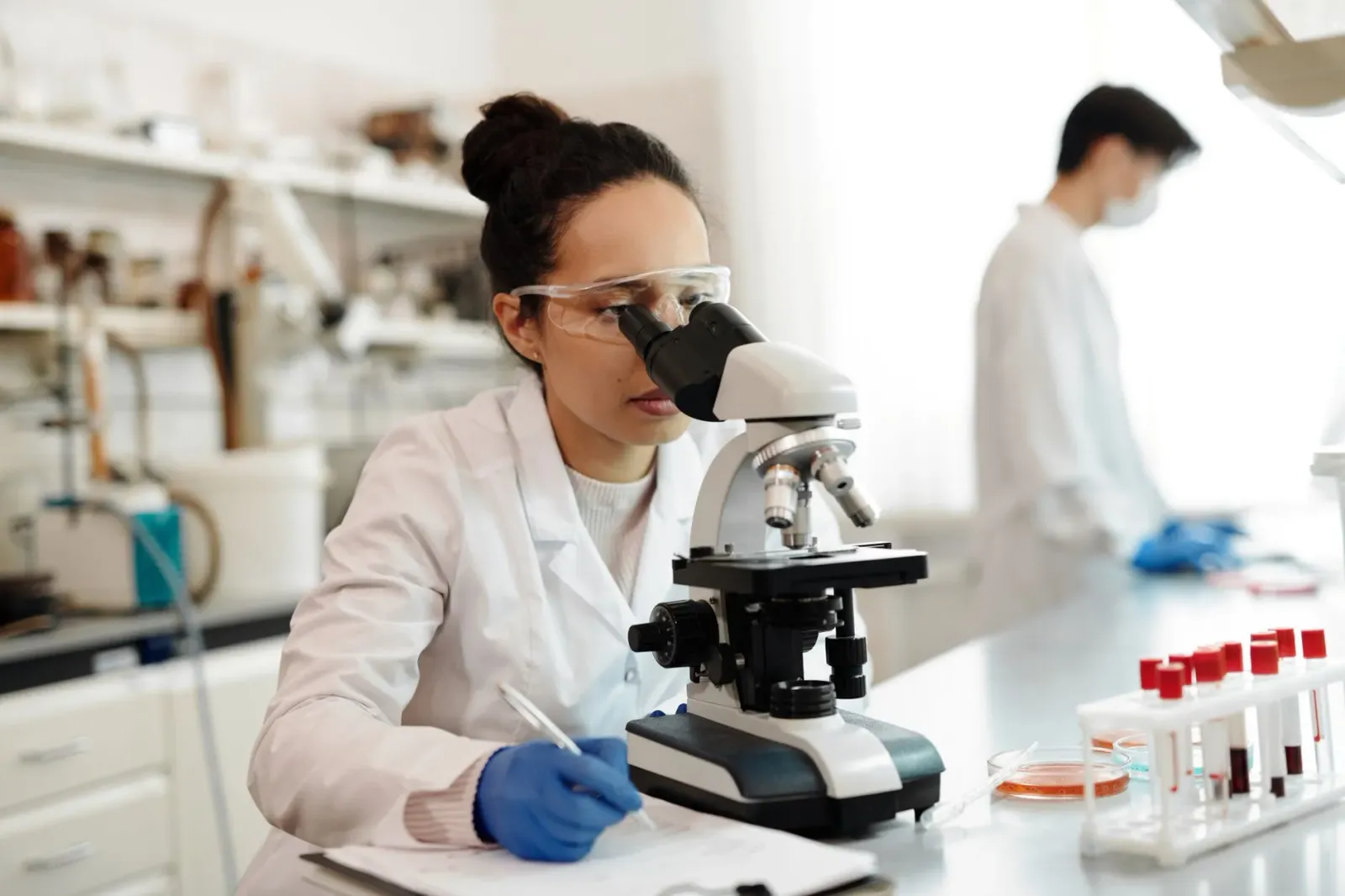 Imajen ida hatudu laboratóriu siénsia modernu ho mikroskópiu no estrutura DNA iha tela, ne'ebé simboliza peskiza siénsia no t