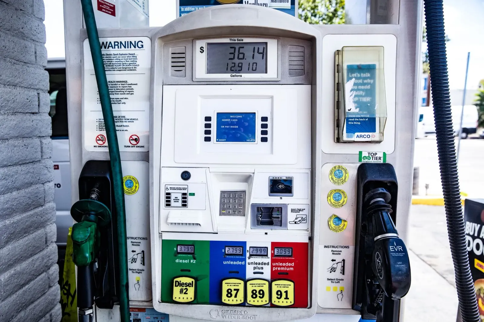 Ema ida iha estasaun gasolina haree prezu gasolina iha painél boot, ho bandeira Amerika iha kotuk, hatudu prezu ne'ebé monu.