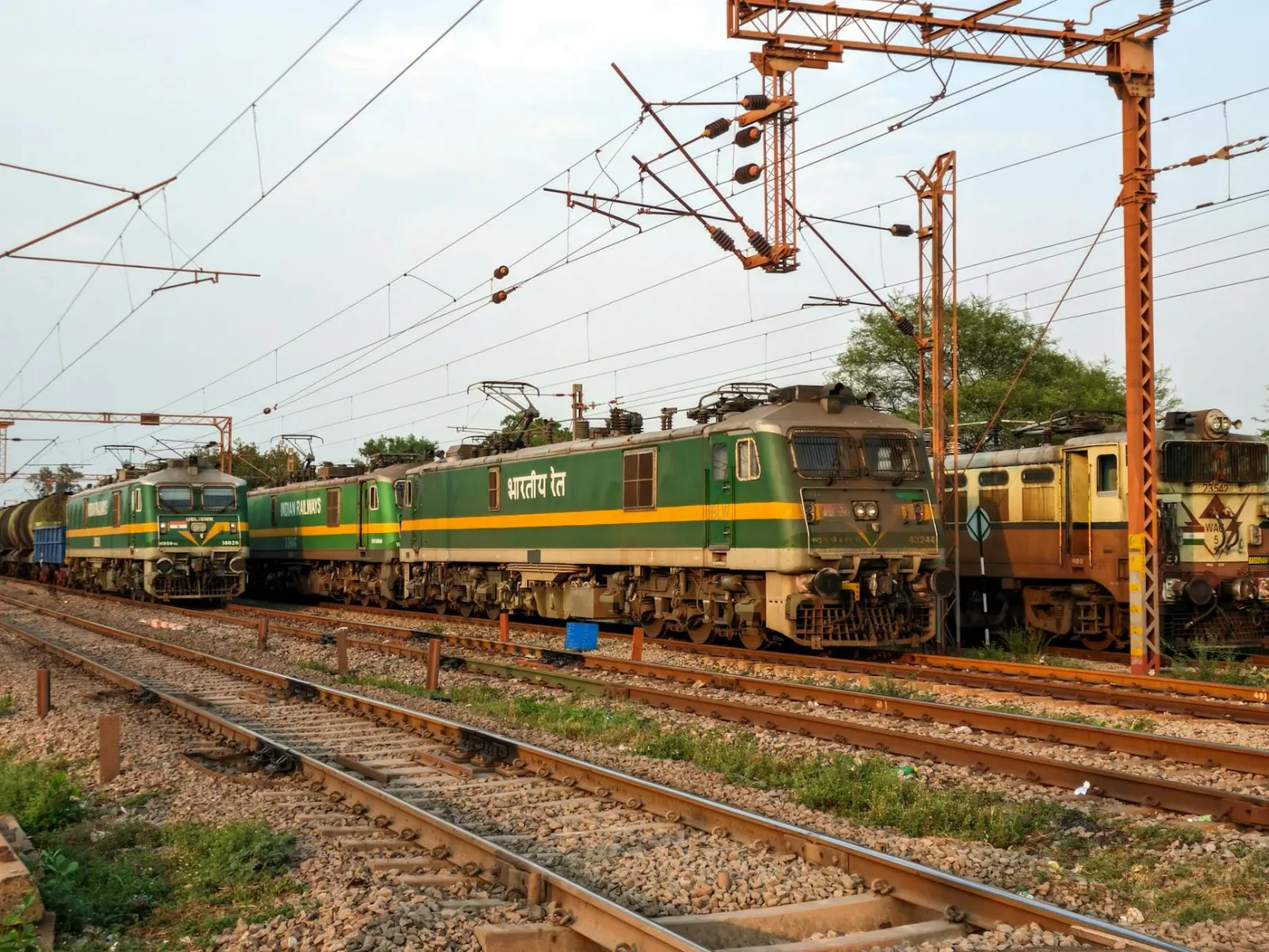 Imajen tren karga Indian Railways ho silinder LPG iha fundu, no dokumentu eleisaun iha meza, simboliza tolu notisia ne'ebé ko