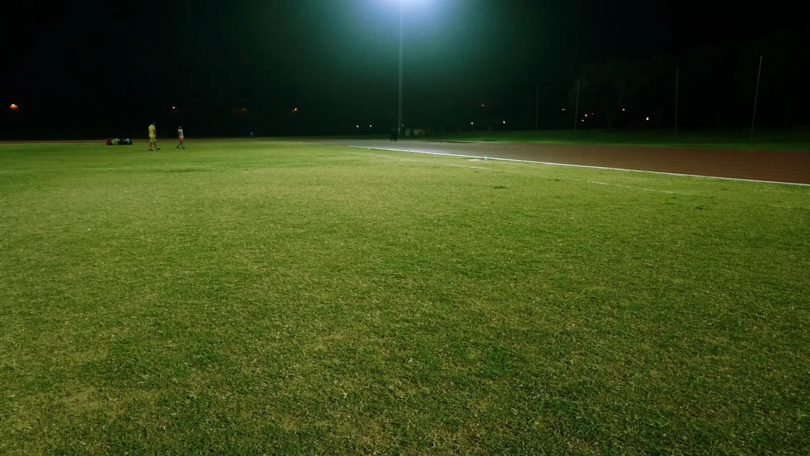 Imajen parke futebol iha Nova Iorke ho luz kalan, ema barak jogu hamutuk iha kampu verde, ho edifísiu sidade iha kotuk, atmos