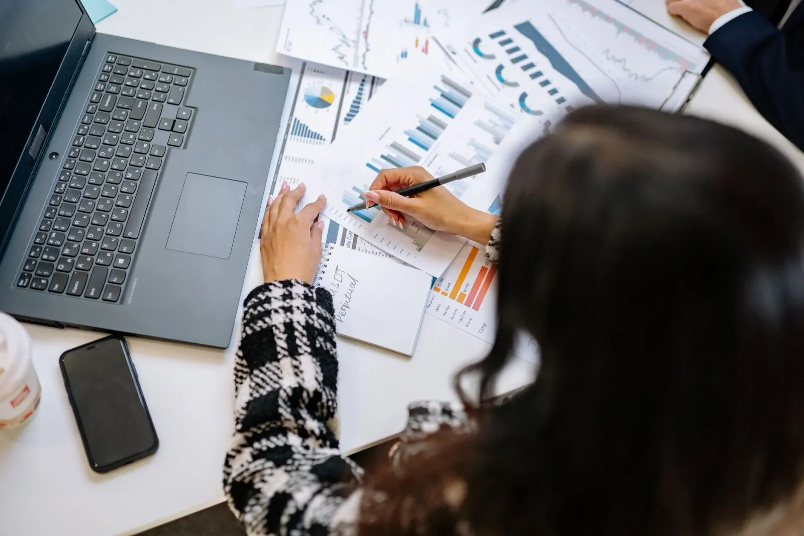 Imajen ida hatudu ema ida ho roupa formal haree dokumentu finanseiru no kalkuladór iha meza, ho naran KPMG no gráfiku iha kot