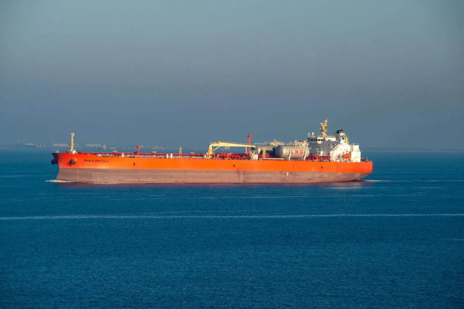 Imajen husi tanker LNG ida ne'ebé para hela iha tasi, ho bandeira nasaun sira no nuvem tempestade iha loro, hanesan simbolu b