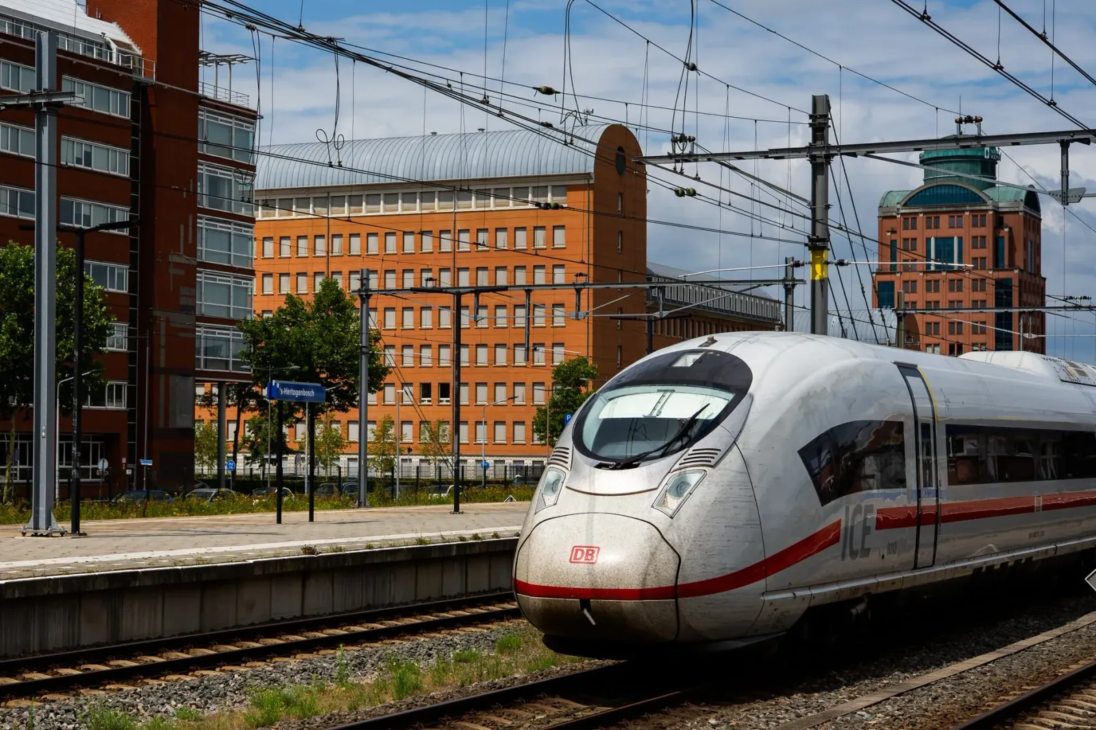 Imajen hatudu sítiu reserva tren iha laptop no smartphone, ho fundo hanesan estasaun tren iha Europa, ne'ebé hatudu performan