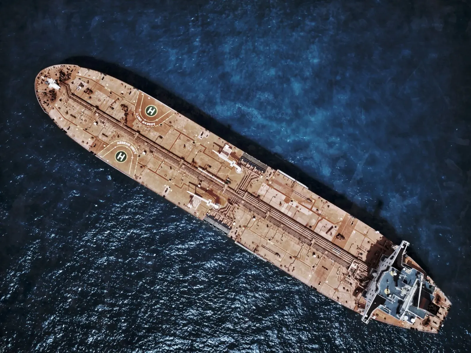 Imajen husi estreitu Hormuz ho tanker petróleu no navy EUA iha tasi, hatudu kontrola rota enerjia global.