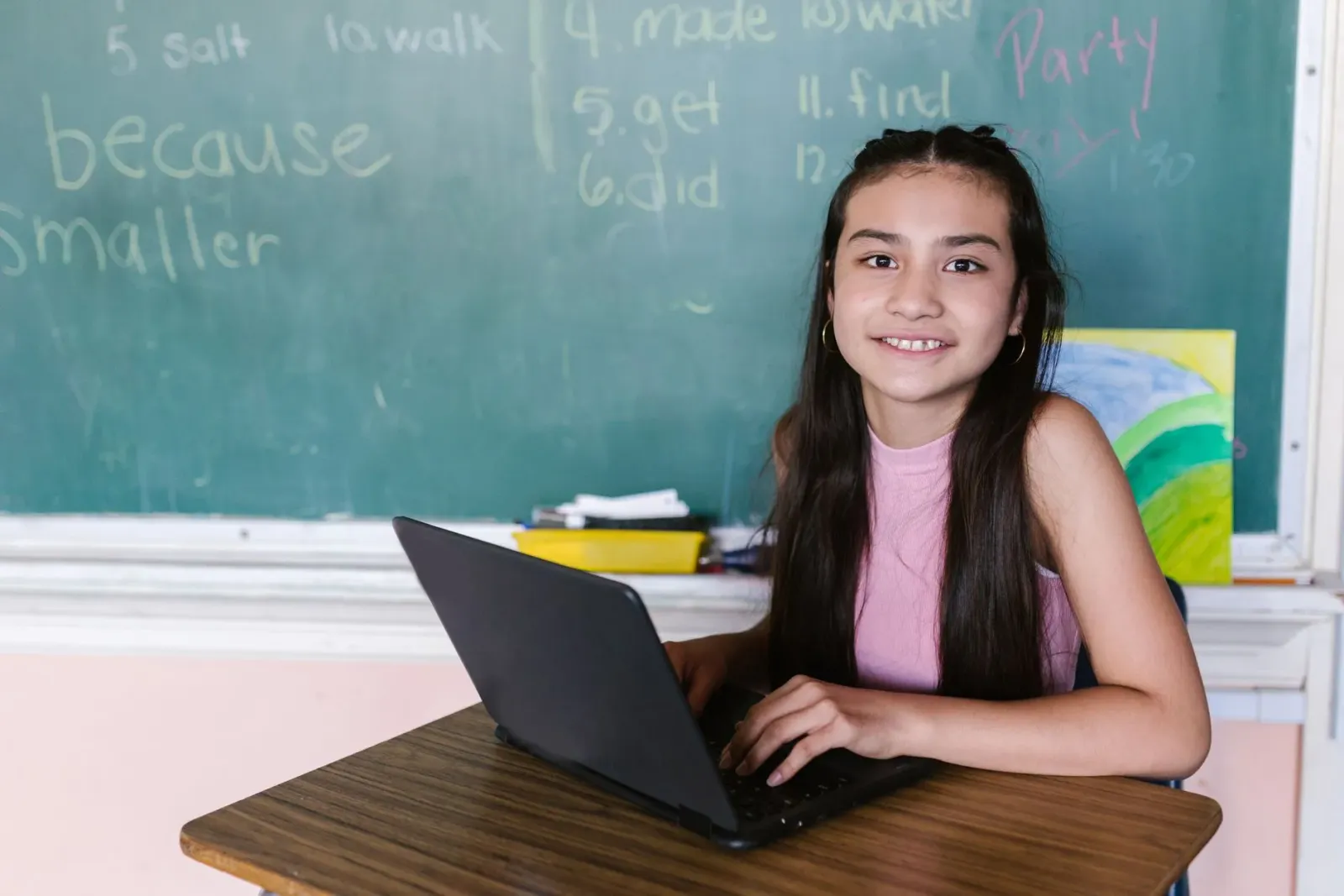 Estudante sira uza laptop iha sala aula, ho sorrisu iha sira-nia oin, hatudu katak teknolojia ajuda sira aprende ho di'ak no 