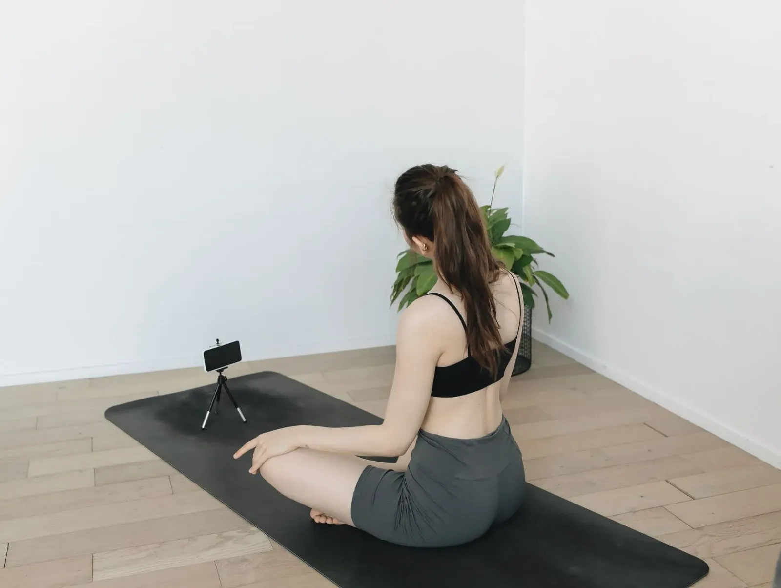 Ema ida prátika yoga iha sala, ho smartphone iha oin hatudu postura, teknolojia AI ajuda korrije movimentu.