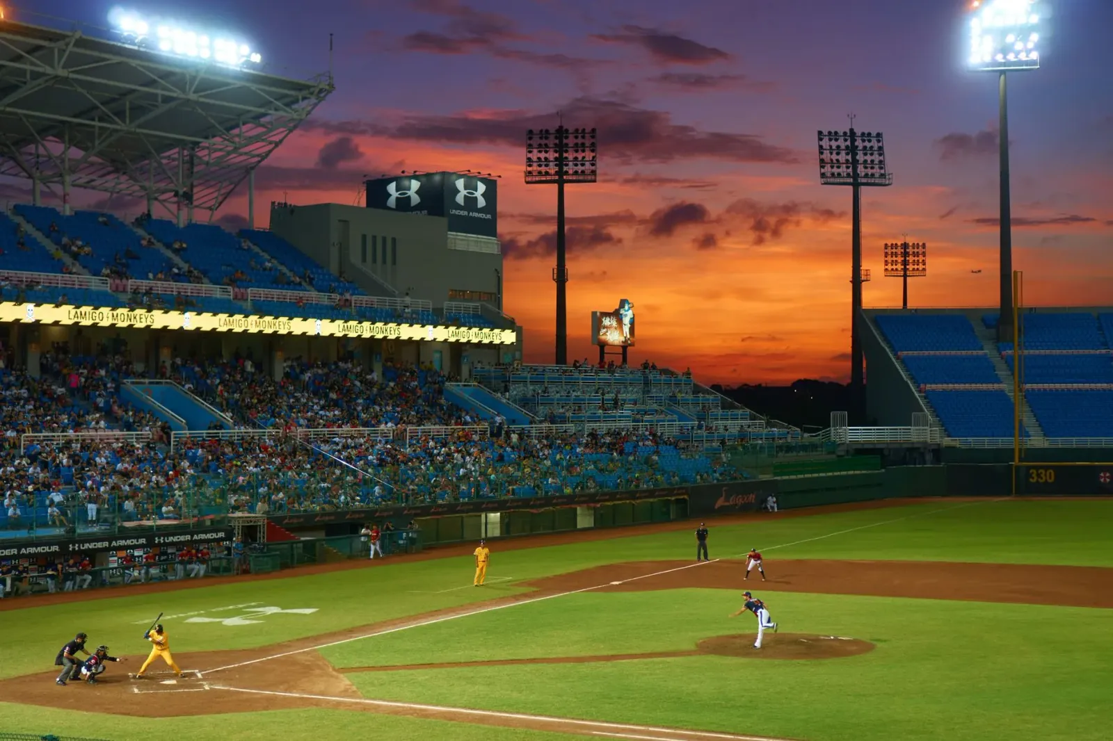 Imajen husi estadiu baseball ho ema barak iha kadeira, ho letra 'Faith & Family Night' iha monitor boot, iha kalan ho luz neo