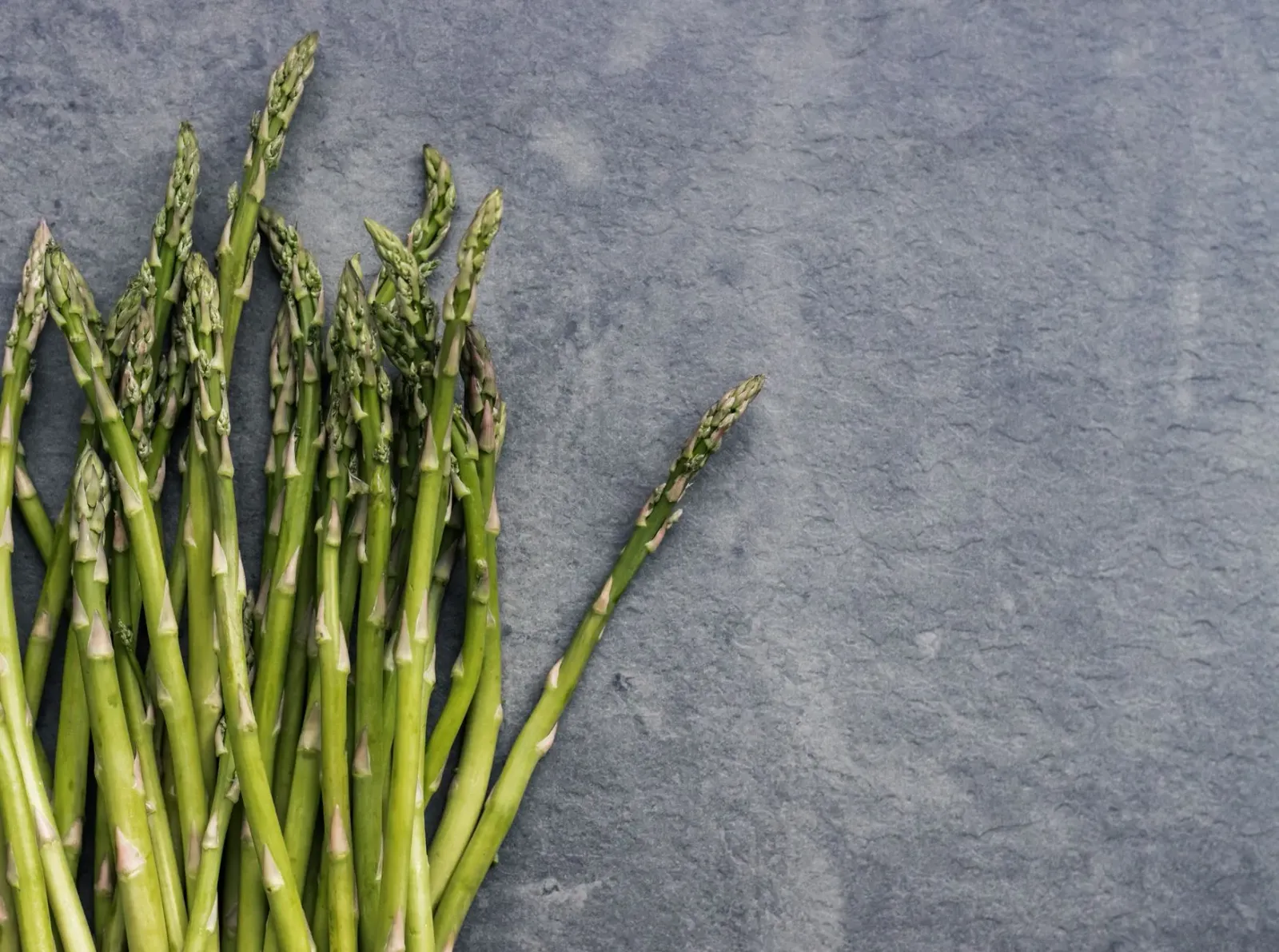 Imajen ida husi asparagus fresku no ai-han green seluk iha meja, simboliza saúde simples no nutrisaun baratu.