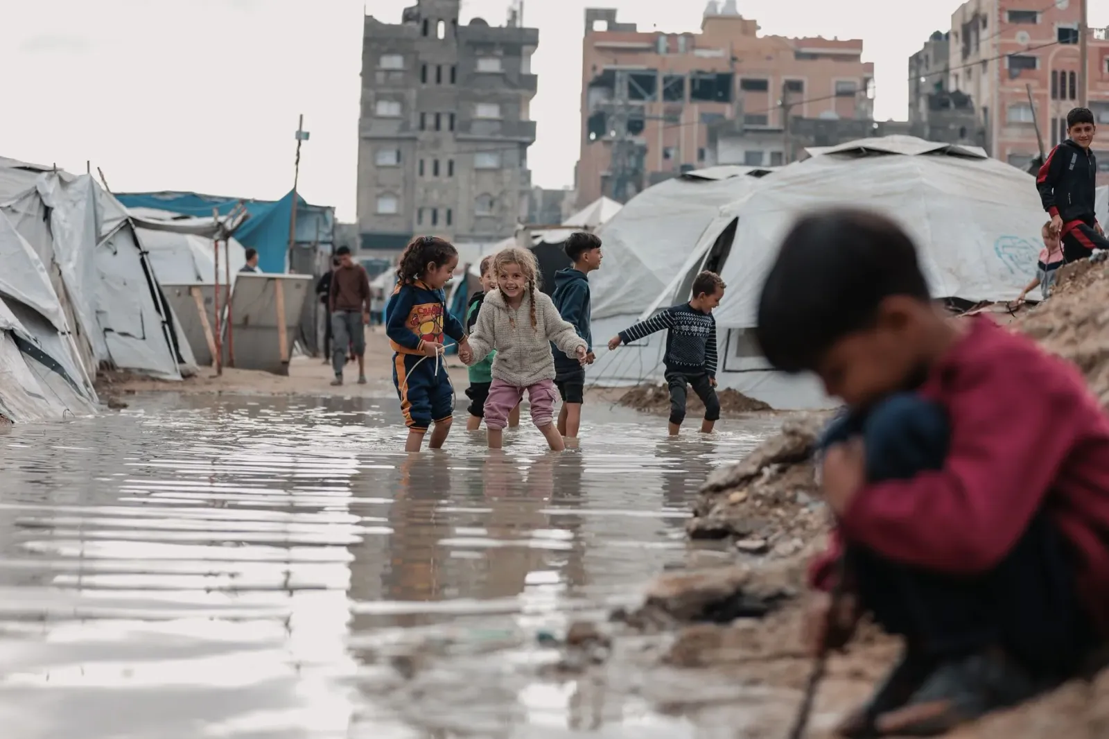 Imajen ida ne'ebé hatudu labarik sira iha Gaza ho ambiente destruidu, ho bandeira UN iha kotuk, nune'e mos livru relatoriu UN
