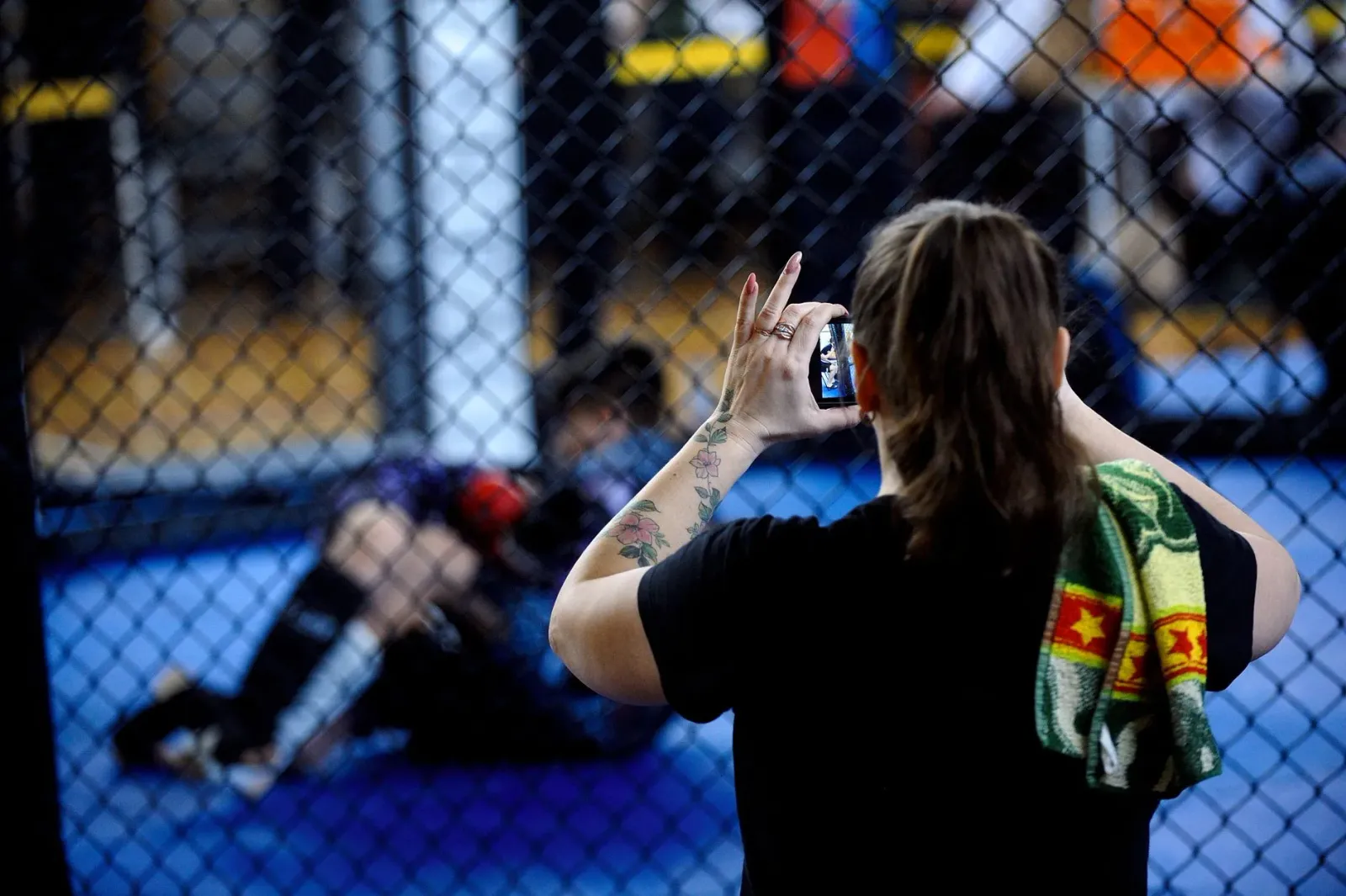 Imajen ida hatudu Cris Cyborg, kampiaun lendária MMA, iha okos lus brilhante, hamriik iha okos PFL cage, ho ninia rosto seriu
