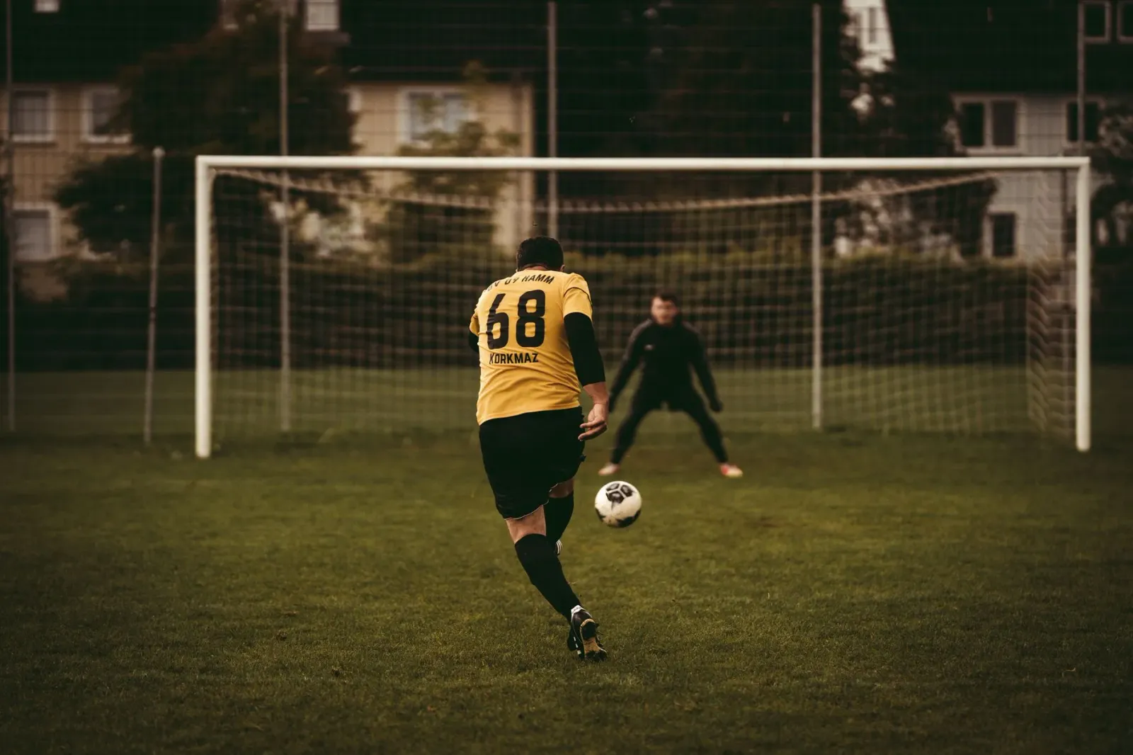 Jogador xuta penalty iha Mundiál Futebol 2026 ho goleiru prontu atu defende, iha estádiu cheia ho ema