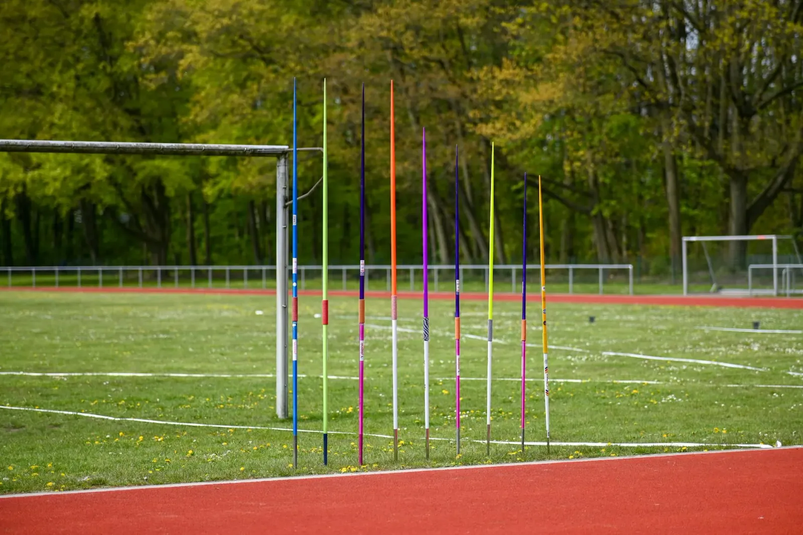 Imajen hatudu elementu desportu Asia: atleta lansa dardo iha estádiu, tela filmu Peddi ho Ram Charan, no logu Sportskeeda, ha