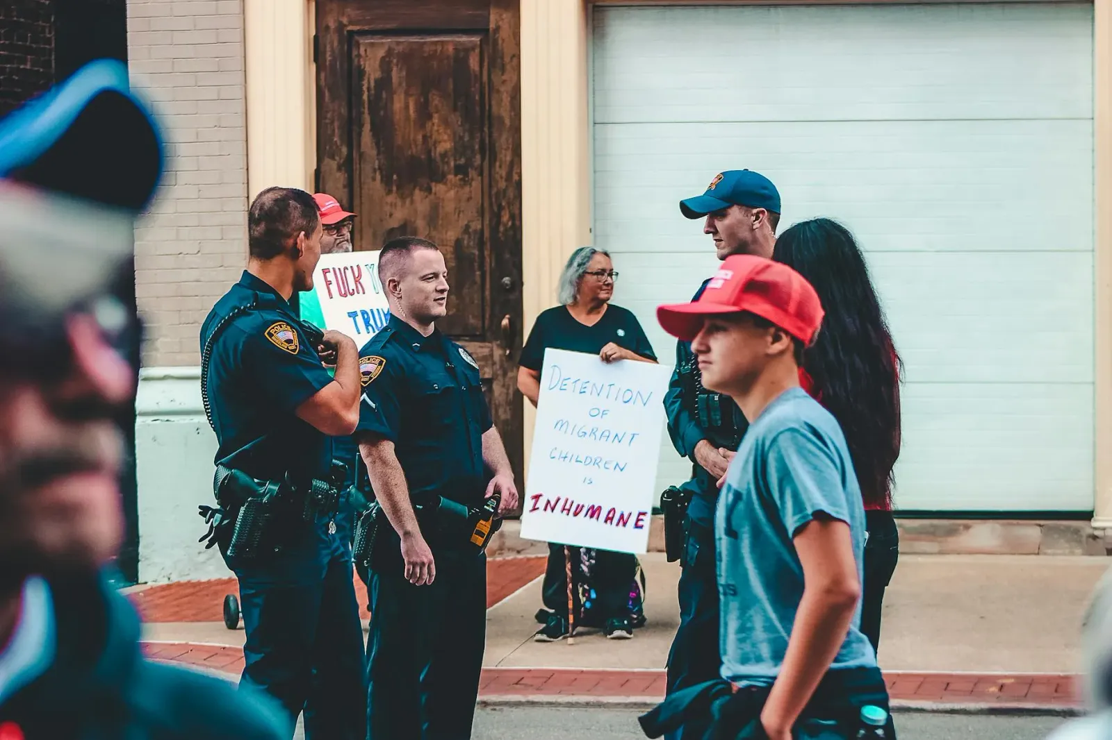 Imajen hatudu ema barak protesta iha liur husi sentru detensaun ICE iha New Jersey, ho faixa no kartás, no jornalista ida iha
