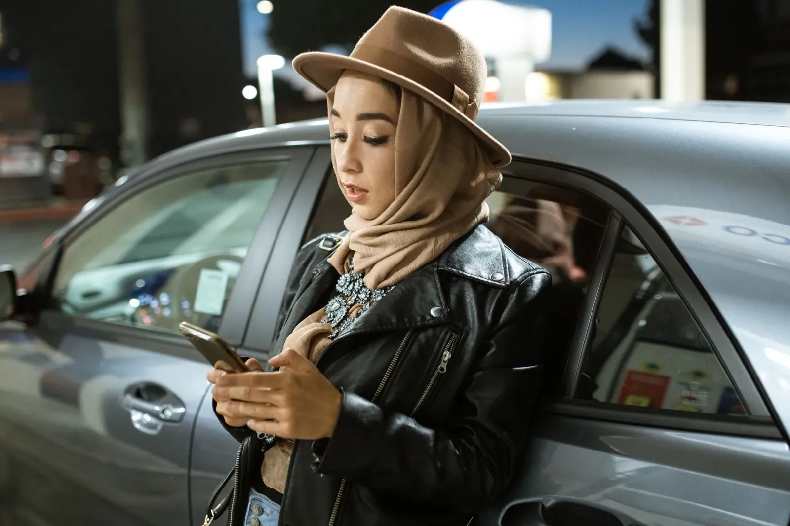 Imajen ida hatudu ema rua uza smartphone, estasaun gasolina iha fundu, no fogo artifísiu iha lalais, ilustra fexting, preu ga