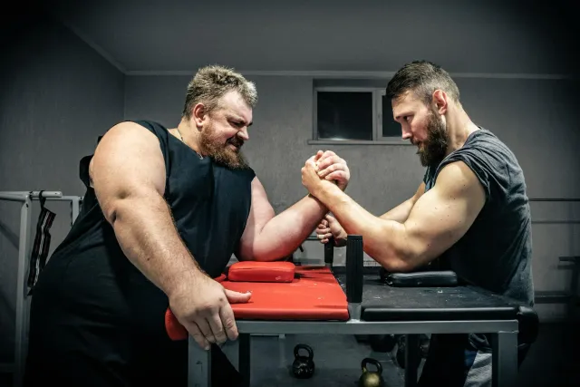 Atleta armwrestling barak tuur iha eventu nasionál iha Gandhinagar, Índia, ho bandeira no ema barak haree hela.