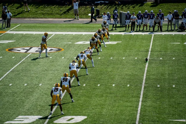 Jogadór LSU Tigers iha kamuflaje jogu kontra McNeese State iha estadio, ho torcedor barak iha fundu, hatudu emosaun no intens