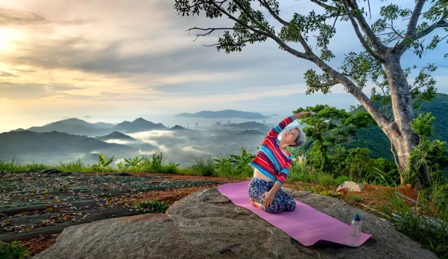 Feto ida ho idade 70+ hamriik ho sorrisu iha natureza, halo ezersísiu simples – simboliza liberdade husi monitorizasaun saúde