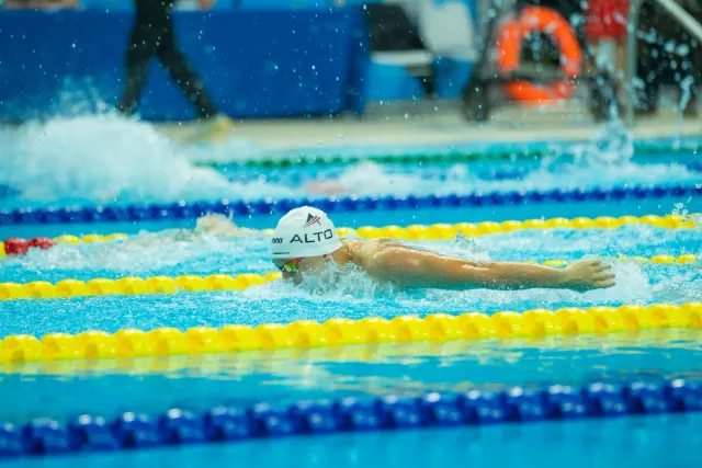 Atleta júnior sira iha piscina no pista korrida, ho mídia stream iha fundo, simboliza futuru desportu no rekonhesimentu