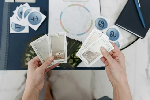 Ema ida tuur iha meza, ho karta tarot no horoskopu espallada, no iha fundu, imajen atleta sira hanesan Simone Biles no Jonath