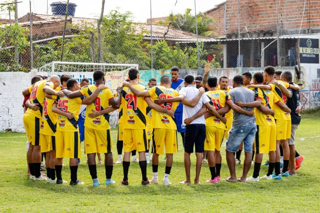Jogador futebol sira hamutuk iha sirkulu, treinador ko'alia ho di'ak, iha segundu planu TV hatudu partida FIFA Mundial 2026 K