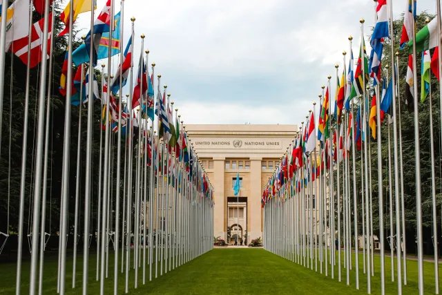 Imajen ne'ebé hatudu diplomatas husi Iran no EUA hamriik iha meja negosiasaun iha Geneva, Suisa, ho bandeira nasaun rua iha t