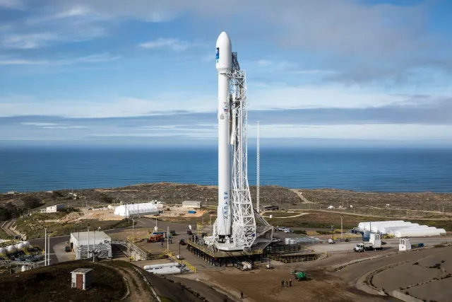 Imajen ida ne'e hatudu foguete SpaceX lansa hela iha loron, ho jogu portátil Lenovo Legion Go iha liman, no ema Yindjibarndi 