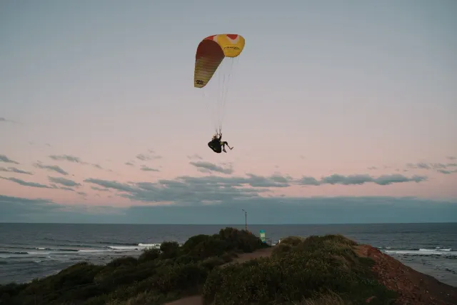 Ema ida paragliding liu husi klifu iha Wales, iha loron sele, ho foho no tasi iha okos.