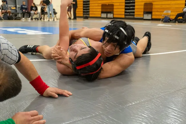 Imajen ida husi feto eskola sekundária ho uniforme wrestling iha partida, ho espresaun determinadu, iha ambiente seguru no ko