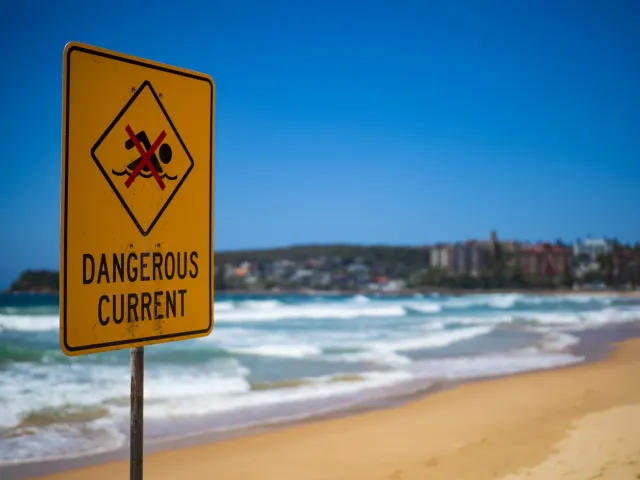 Plaka avizu tubaraun iha tasi-ibun Coogee Beach, Australia, ho sinal vermellu no textu 'Shark Warning' iha fundu tasi no lale