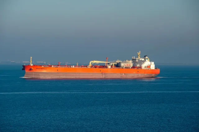 Imajen husi tanker LNG ida ne'ebé para hela iha tasi, ho bandeira nasaun sira no nuvem tempestade iha loro, hanesan simbolu b