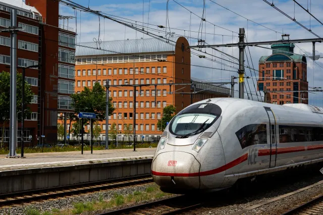 Imajen hatudu sítiu reserva tren iha laptop no smartphone, ho fundo hanesan estasaun tren iha Europa, ne'ebé hatudu performan