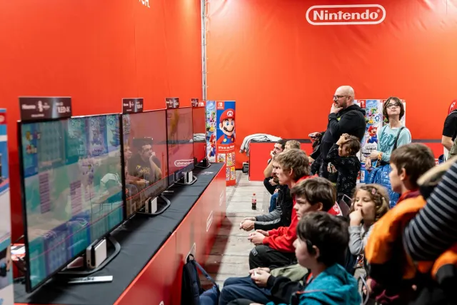 Imajen ida ne'ebé hatudu palco boot ho letras Xbox no PlayStation iha eventu Summer Game Fest, ho ema barak tuur hela iha aud
