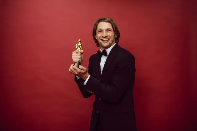 Estátua Oscar iha eventu red carpet, ho fundu neon no ema sira haree ho admiracao
