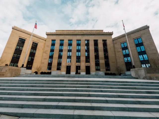 Imajen ida husi edifísiu Federal Reserve iha Washington D.C., ho bandeira americana no mikrofonu sira iha mesa, simboliza kon