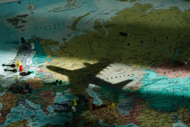 Imajen ida hatudu gráfiku prezu bilhete aviária ne'ebé tun, ho mapa mundu iha kotuk, simboliza ligasaun entre ekonomia no geo