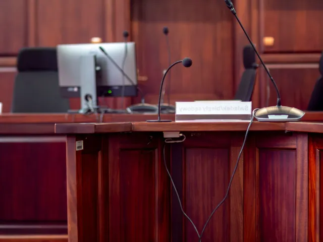 Imajen ida hatudu tribunal ho juiz no advogadu sira koalia kona-ba AI iha indústria entretenimentu, ho komputadór no dokument