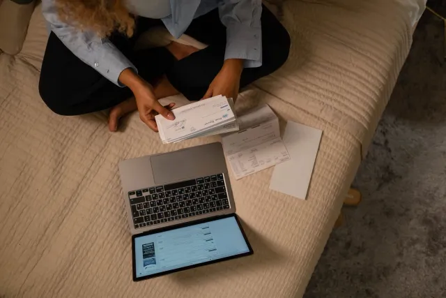 Ema ida haree fatura subskrisaun iha laptop, ho espresaun preukupadu, iha meja ho dokumentu no kafé