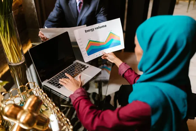 Imajen ida hatudu ema negósiu indianu sira tuur hamutuk iha meja konferénsia, ho dokumentu no planu kona-ba enerjia, finansa 