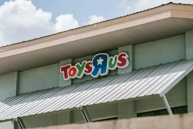 Imajen ida hatudu loja brinquedu Toys R Us no loja kafé Starbucks iha area komersial, ho ema sira la'o hela, simboliza mudans