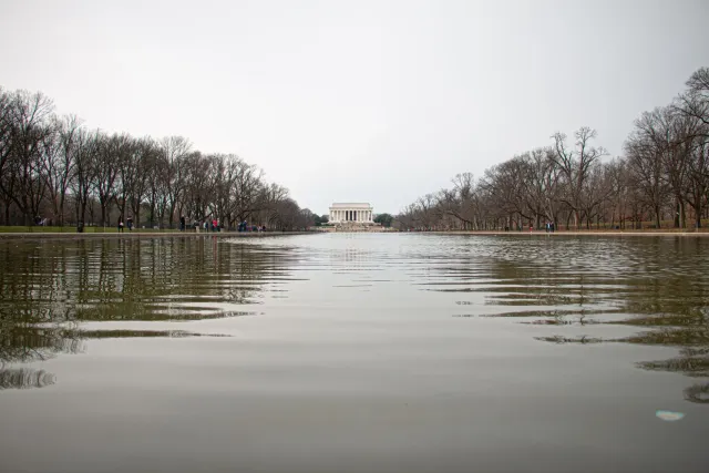 Imajen ida hatudu Lincoln Memorial Reflecting Pool ne'ebé muda tiha kór verde, ho ema barak hareé hela, hanesan sinal kona-ba