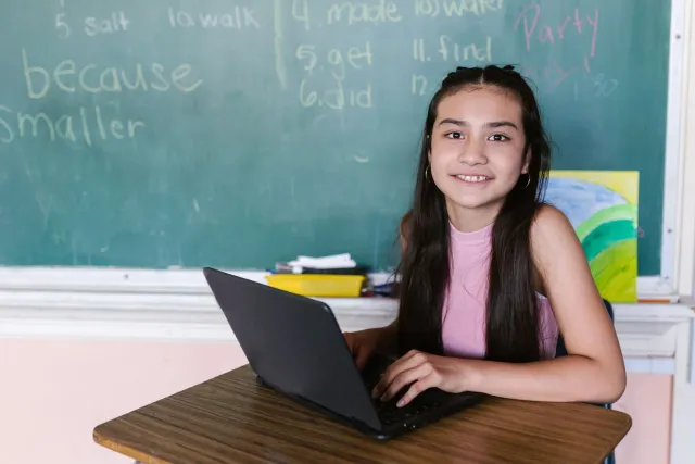 Estudante sira uza laptop iha sala aula, ho sorrisu iha sira-nia oin, hatudu katak teknolojia ajuda sira aprende ho di'ak no 