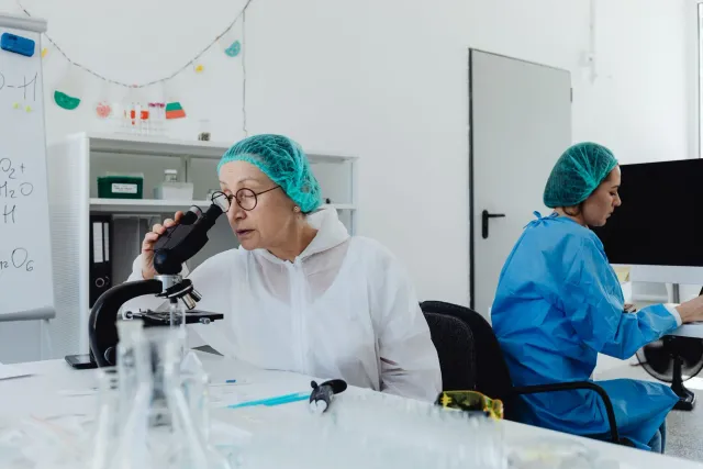 Sientista ida hare liuhusi mikroscópiu iha laboratóriu ho luz ne'ebé fo sente drama, hatudu seriedade no foku ba deskobriment