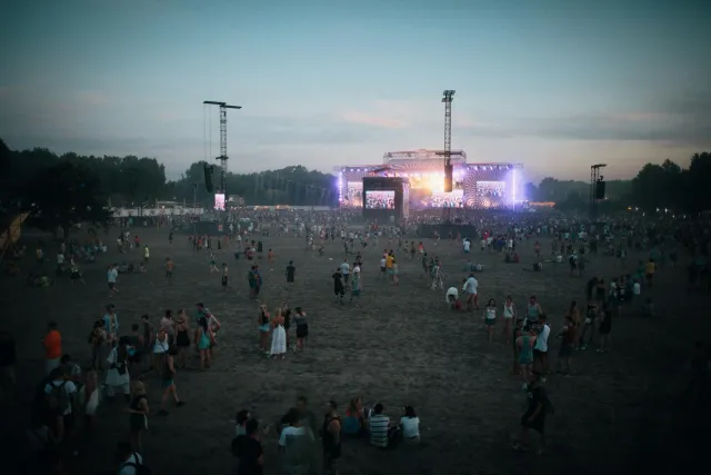 Ema barak hamutuk iha konsertu gratuitu iha parke, ho palco no múzika, hatudu atmosfera alegre no komunidade forte, iha Midla