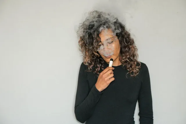 Imajen ida hatudu ema ho vaporizador eletróniku (vape) ho fumus sai husi nia, ho sientista iha fundu hatudu ADN ne'ebé danifi