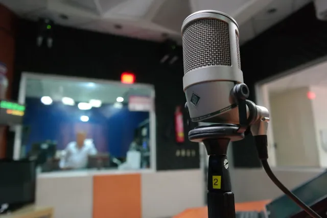 Imajen ida hatudu komentadór desportu ida iha kabina ho mikròfone, hakerek analiza jogu iha televizaun nia tela.