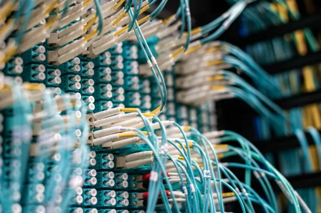 Imajen ida ne'ebé hatudu data-center boot ho luz azul no komputadór sira, ho símbolu seguransa siber iha leten, hanesan repre