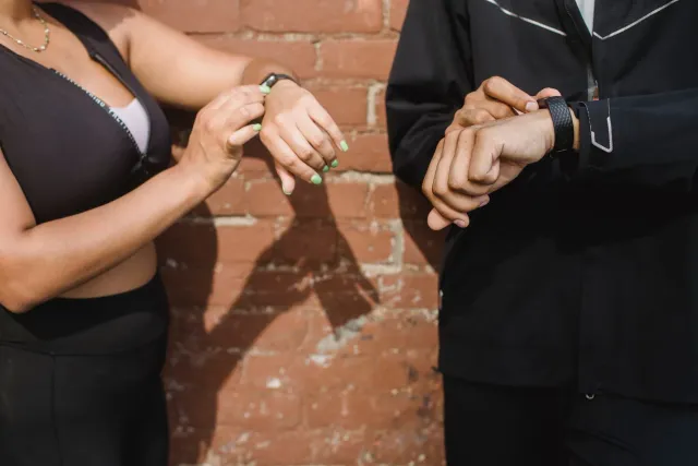 Imajen ida ne'ebé hatudu fitness tracker sira iha meja, ho televizaun ne'ebé hatudu partidu futebol no eventu UFC iha fundu, 