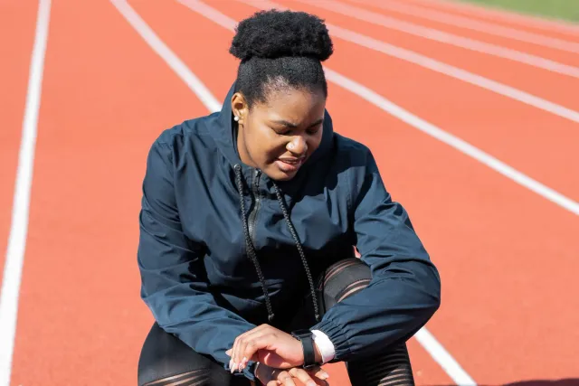 Atleta ida uza smartwatch iha treinu korrida iha estrada, ho dalan no árvore iha fundu, hatudu oinsá teknolojia monitor ajuda