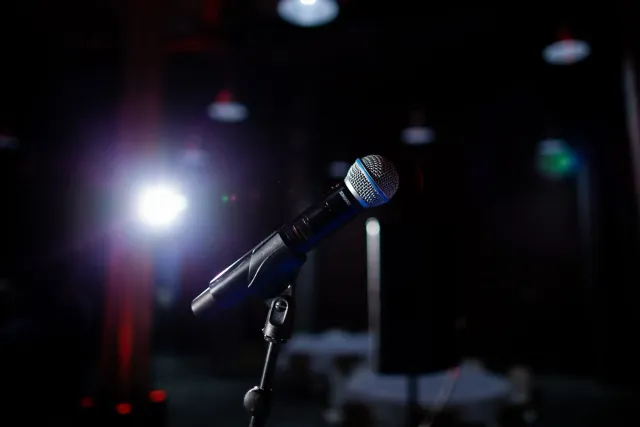 Imajen ida ne'ebé hatudu palco ho logu InfoWars no The Onion, ho luz neon no plateia, hanesan reprezentasaun ba reboot media 