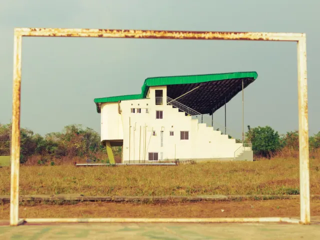 Imajen hatudu obra estadiu ne'ebé seidauk remata ho atleta sira treinu iha fatin seluk, simboliza atrazu no presaun iha mundu